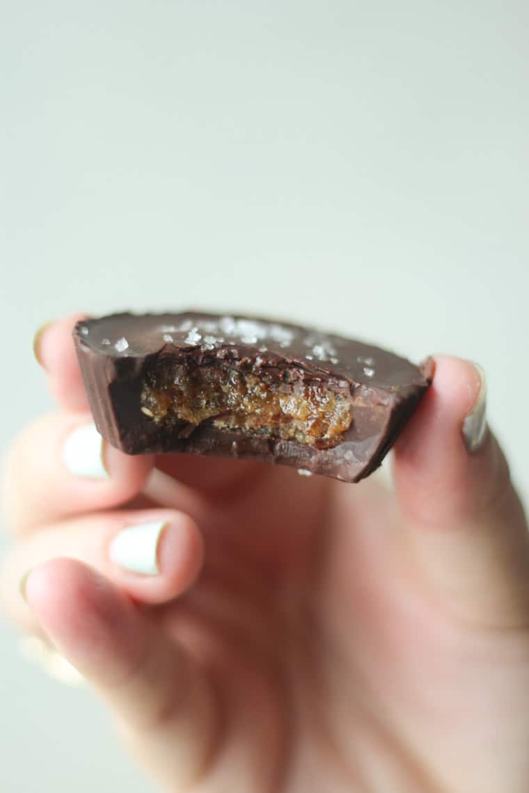 hand holding half eaten vegan chocolate caramel cup topped with flaky salt