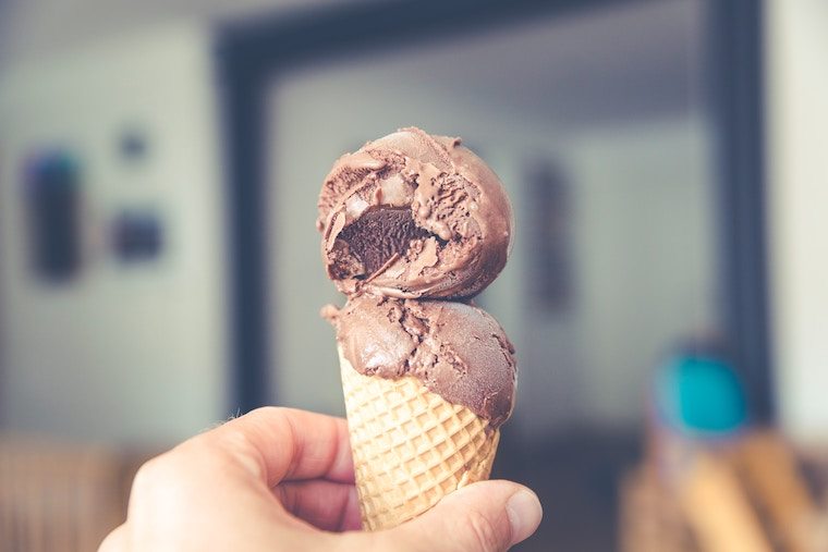 A hand holding up a waffle cone with chocolate ice cream.