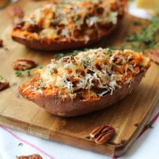 A close up of a baked sweet potato with caramelized onion and apple on a brown cutting board.