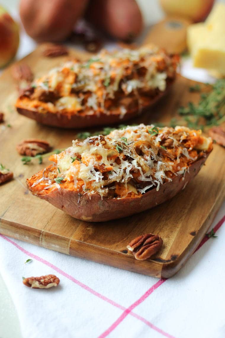 A close up of a baked sweet potato with caramelized onion and apple on a brown cutting board.