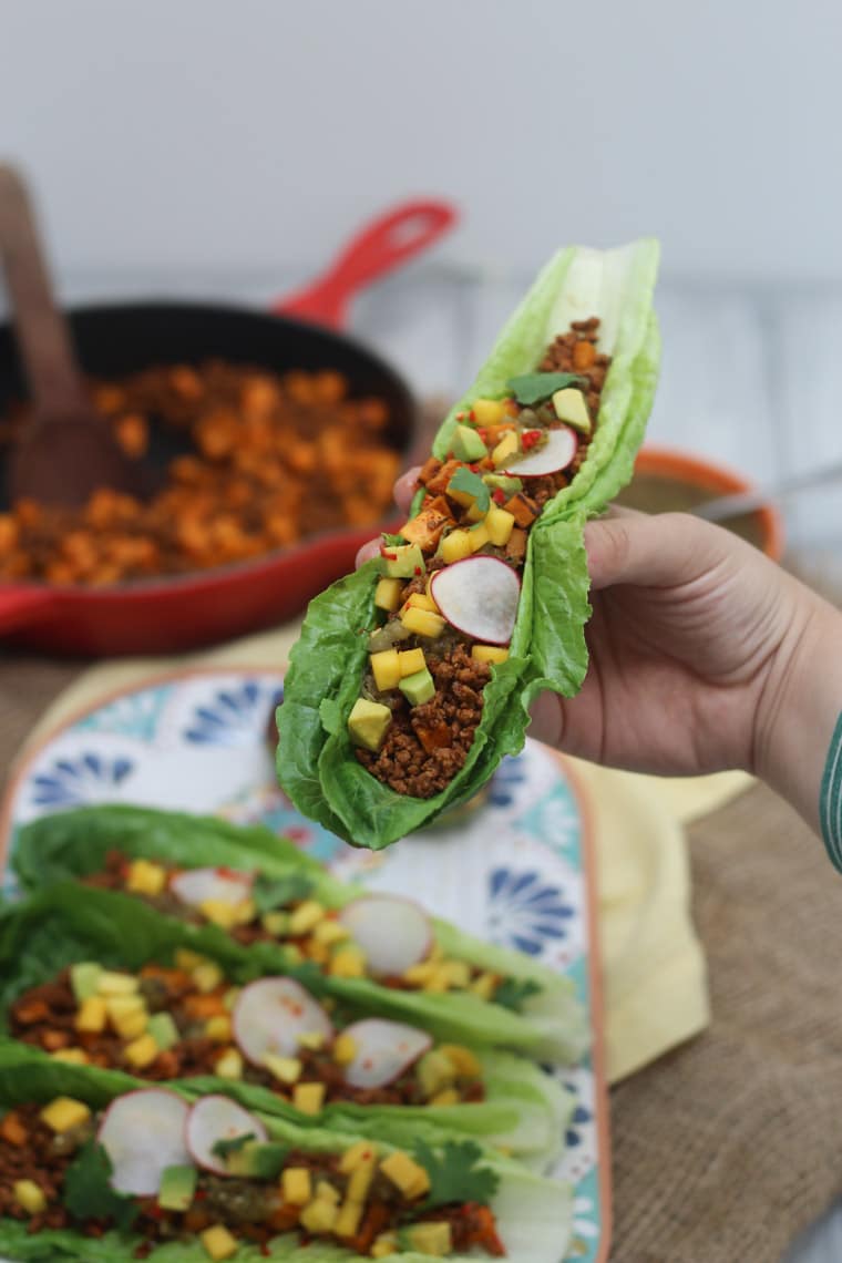 hand holding low fat gluten free paleo chorizo and sweet potato taco garnished with fresh vegetables