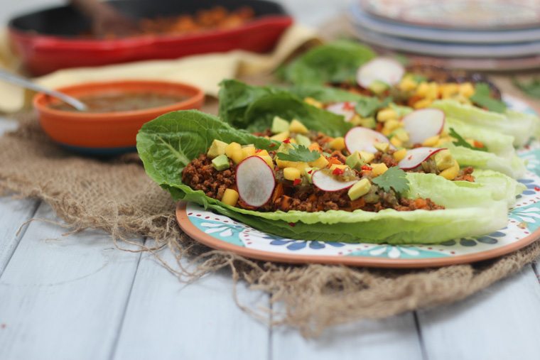 paleo chorizo and sweet potato tacos garnished with fresh vegetables served in lettuce wraps on a floral plate