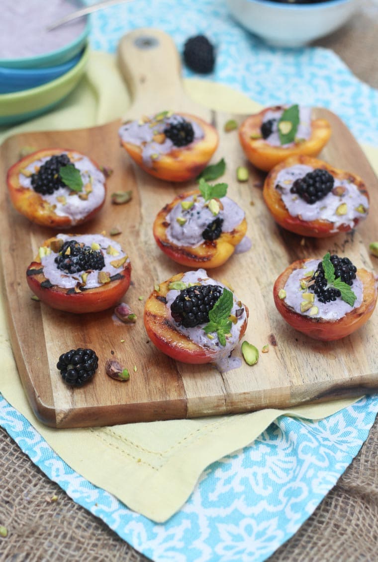 A white serving platter with multiple grilled peaches with blackberry coconut cream inside.