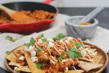 A place of nachos with butter chicken on top.