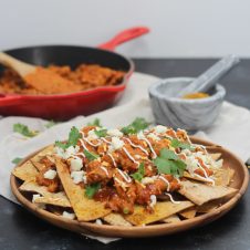 A place of nachos with butter chicken on top.