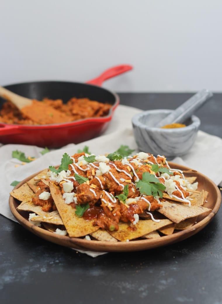 A place of nachos with butter chicken on top.