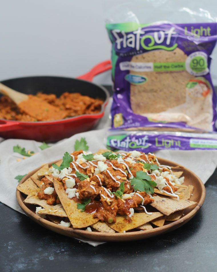 A photo of butter chicken nachos with flatout bread in the background and a skillet of the chicken.