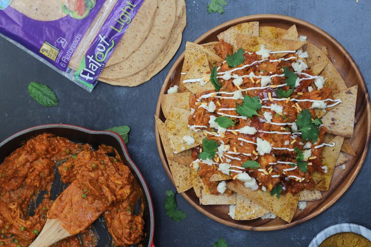 An overhead photo of a plate of indian nachos with sauce drizzled on top and garnish.