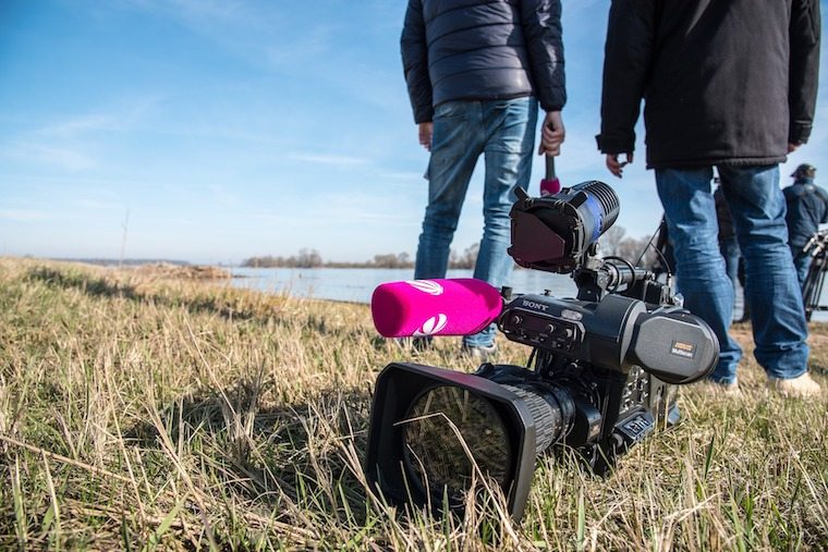 Two people standing in a field with a camera.