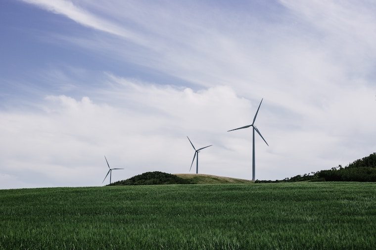 A three windmill on top of a lush green field.