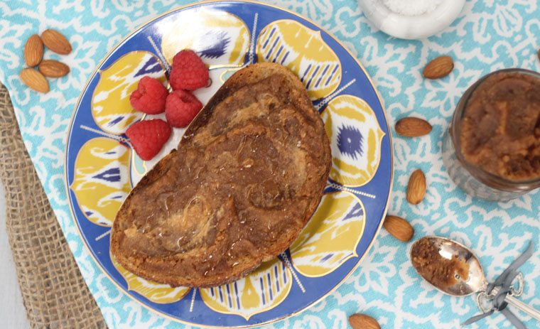 An overhead photo of a table with a blue plate with salted caramel almond butter spread on top with raspberries beside it.