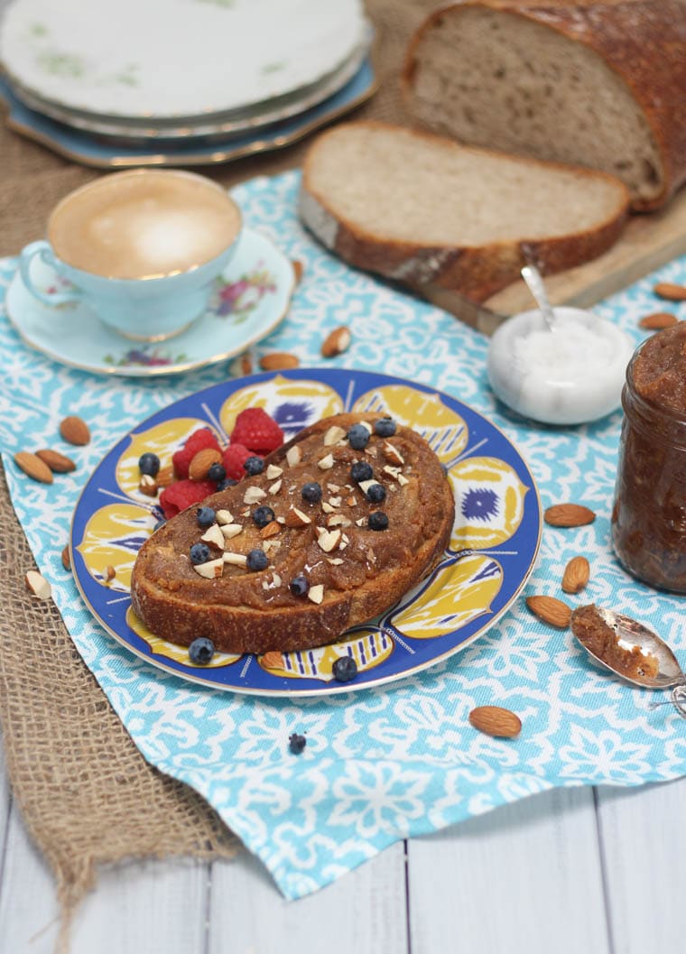 A table with a blue plate with salted caramel almond butter spread on top with blueberries on top.