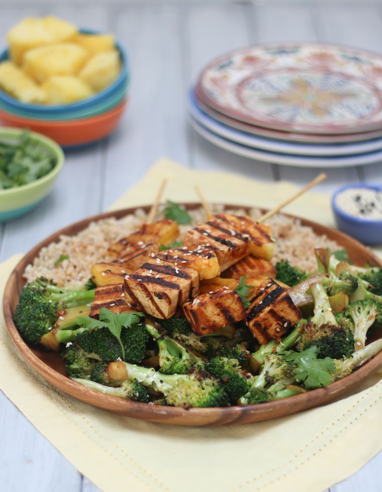 dinner plate filled with spicy tofu and pineapple skewers, rice, and greens