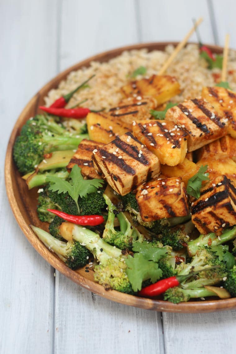 close up of spicy tofu skewers on a dinner plate garnished with cilantro and sesame seeds