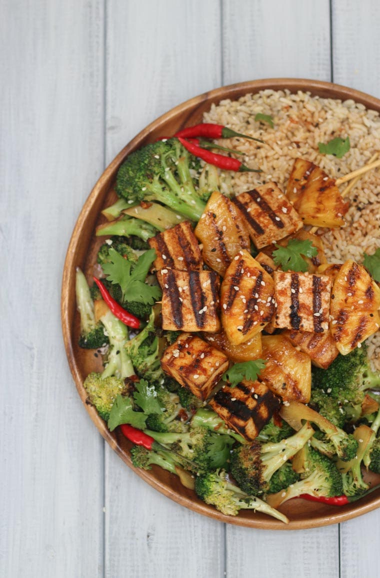 birds eye view of sriracha grilled tofu skewers on a wooden plate served with rice and greens