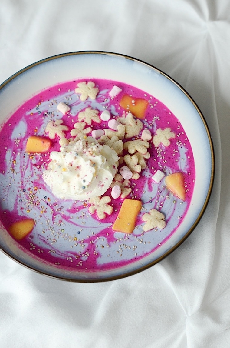 An overhead photo of a pink smoothie bowl with whipped cream.