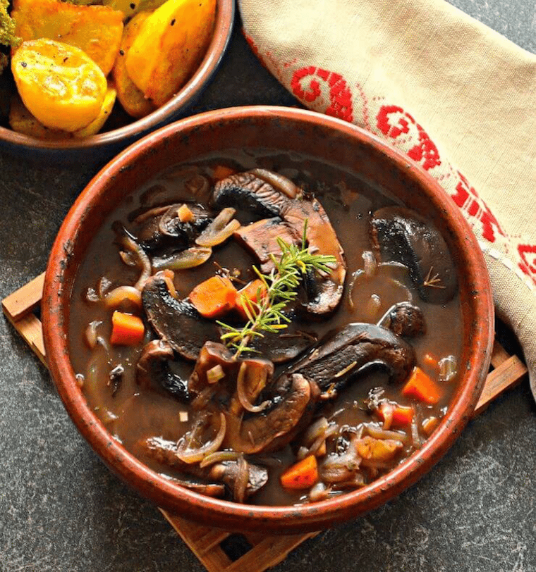 Birds eye view of vegan portobello pot roast garnished with herbs in a red pot.