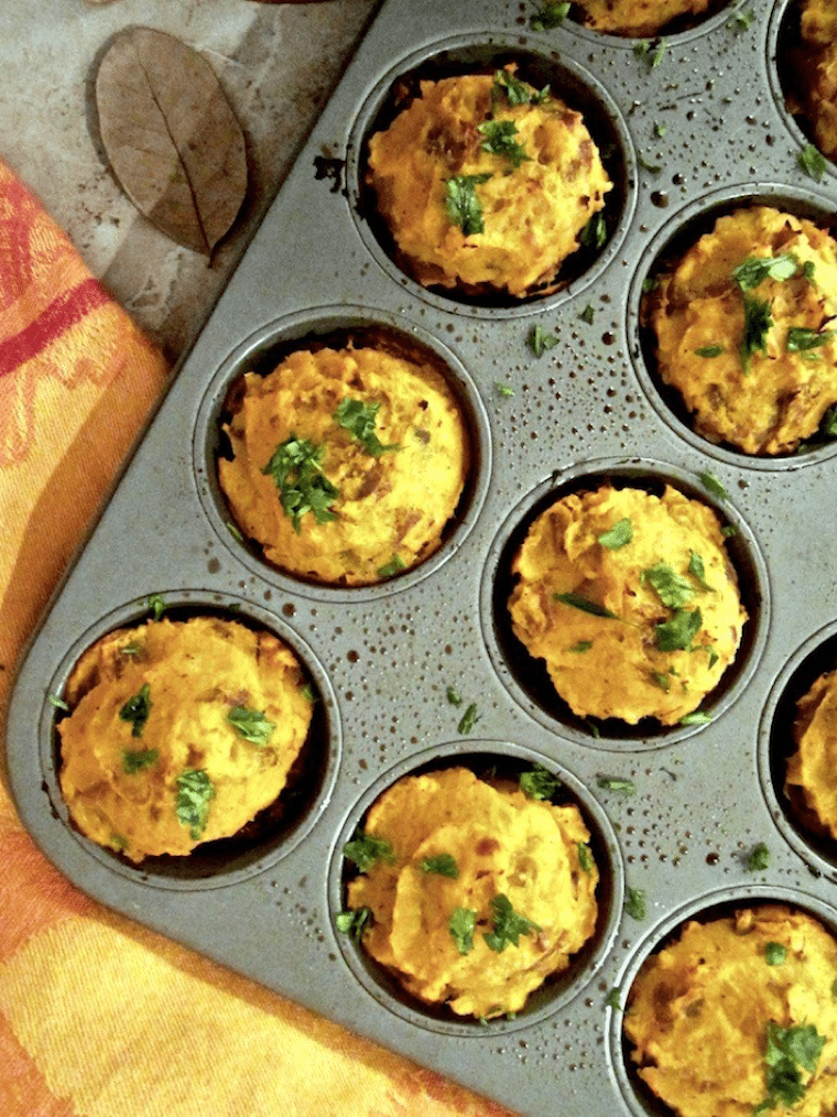 Birds eye view of mini vegan shepherds pies in a muffin tray garnished with fresh herbs.