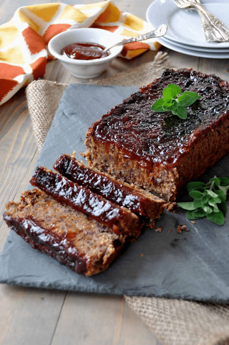 vegan meatloaf cut into slices garnished with fresh herbs on a grey dish