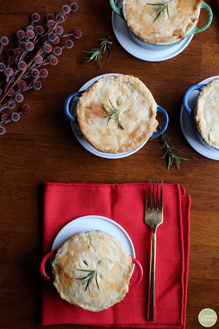 Birds eye view of multiple vegetable pot pies garnished with fresh herbs on a wooden table.