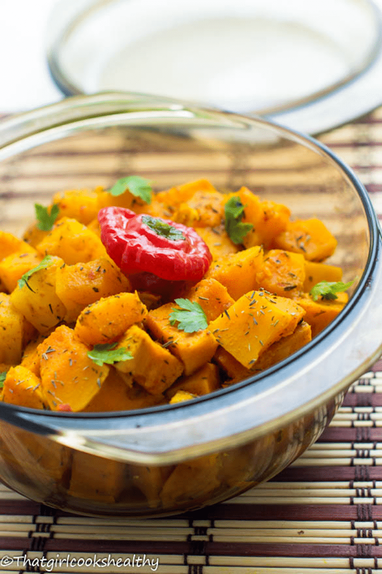 Close up of Caribbean pumpkin curry served in a clear bowl garnished with herbs.