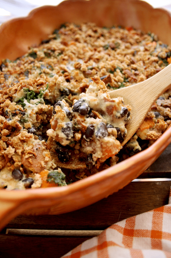 Close up image of vegan sweet potato casserole in an orange casserole dish with a wooden spoon inside.