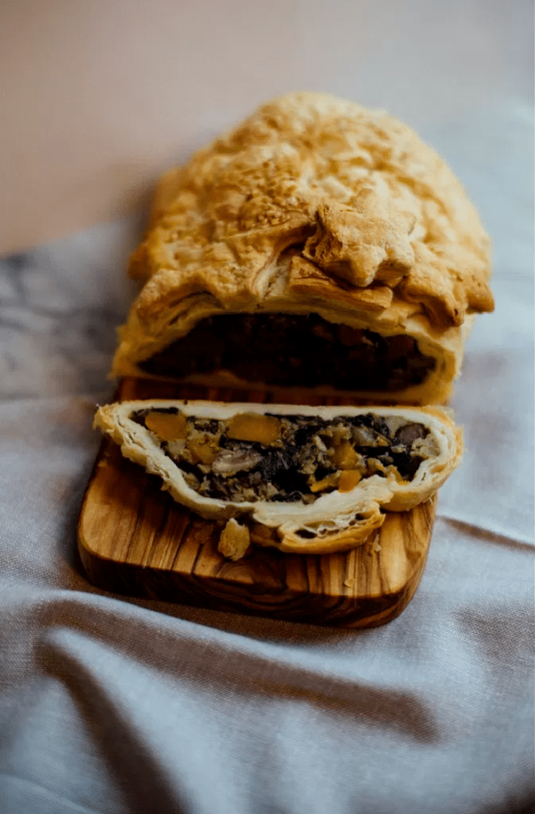 Image of a vegetable wellington dish served on a wooden board with a slice cut out.