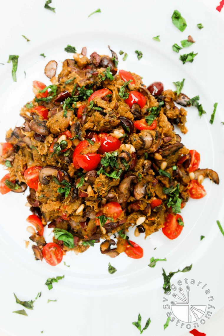 Close up of mediterranean spaghetti squash on a white plate garnished with herbs and tomatoes.