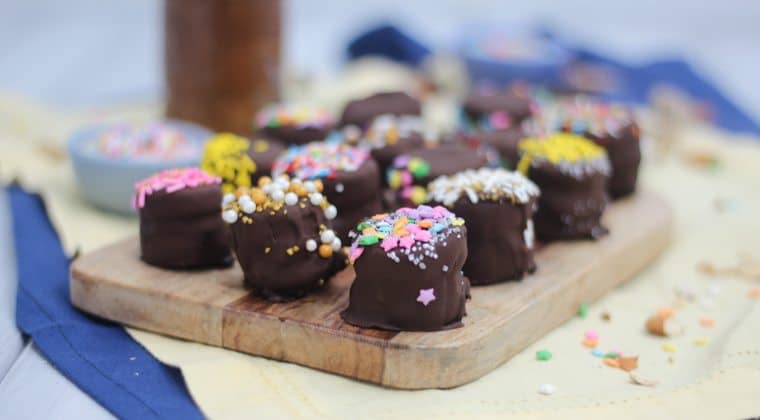 gluten free chocolate dipped banana bites stuffed with caramel almond butter on a wooden surface topped with sprinkles