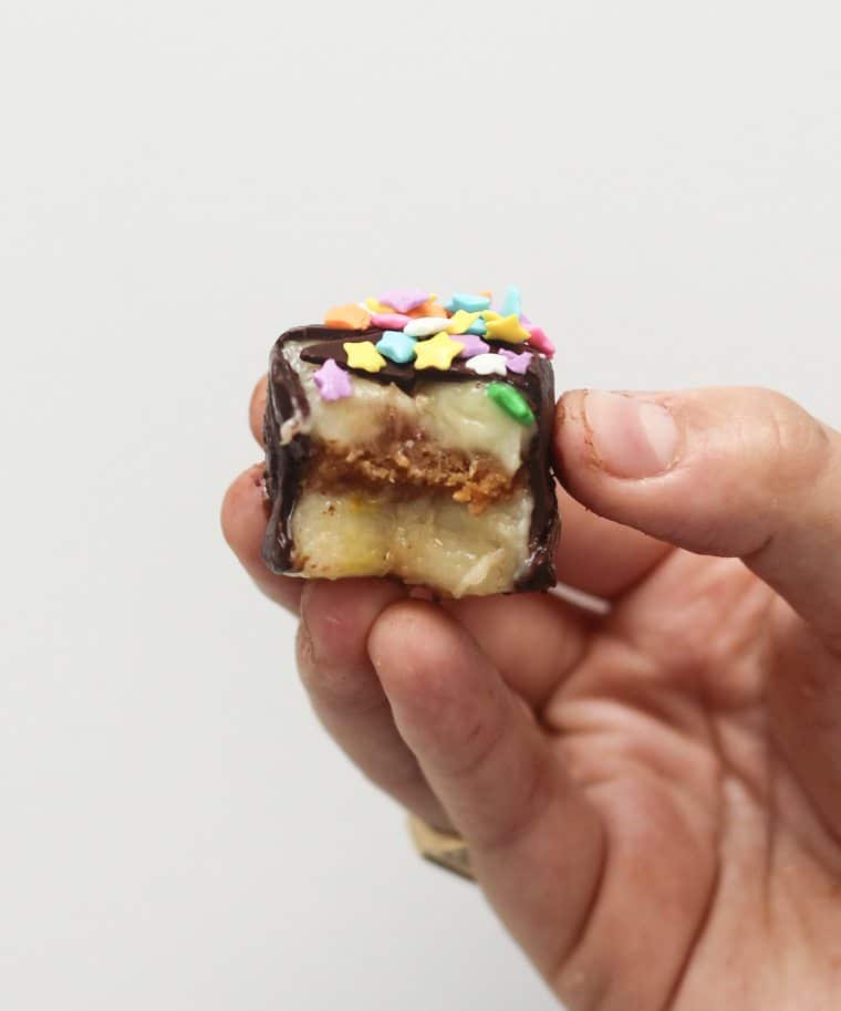 hand holding a half eaten chocolate banana bite stuffed with caramel almond butter topped with sprinkles