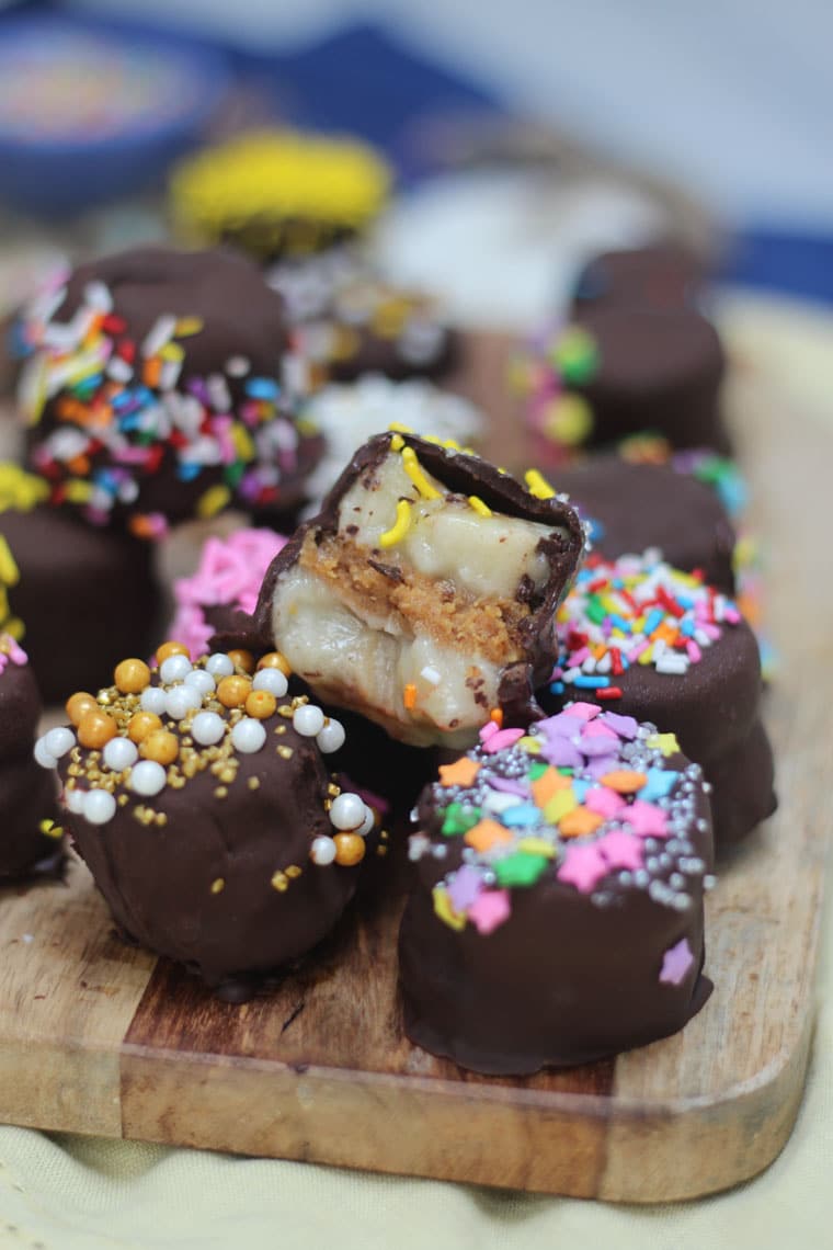 multiple paleo vegan chocolate dipped banana bites on a wooden counter topped with sprinkles