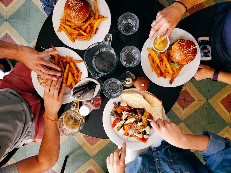 An overhead photo of a table with four plates of takeout including fries and burgers.