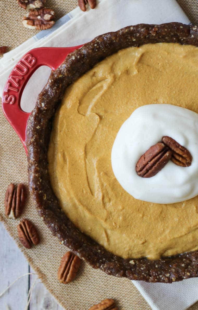 Pumpkin pie in red dish garnished with pecans.