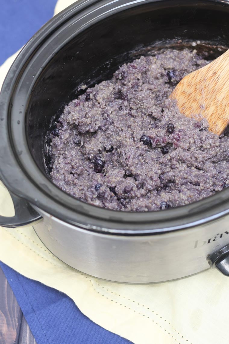 Blueberry quinoa inside of a slow cooker with a wooden spoon inside.
