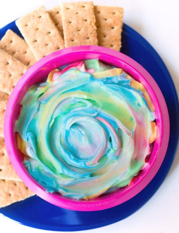 A bowl of pastel rainbow coloured dip with crackers beside it.