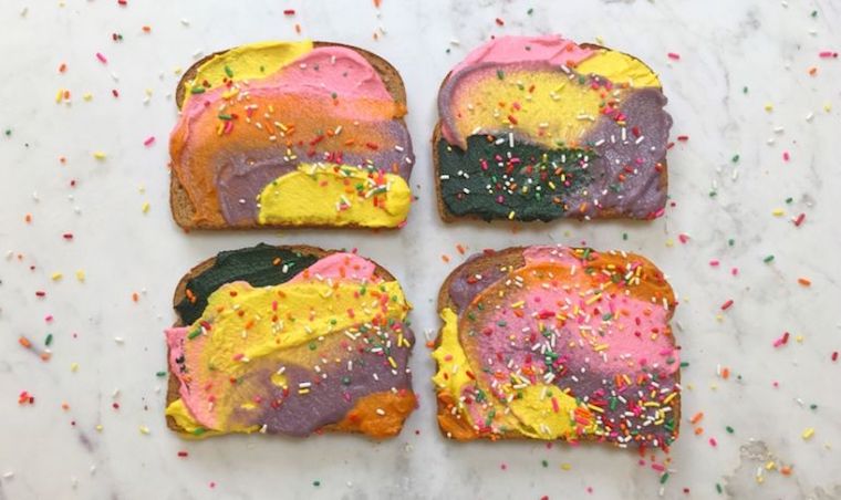 Four pieces of toast with pastel coloured spread with rainbow sprinkles on top.