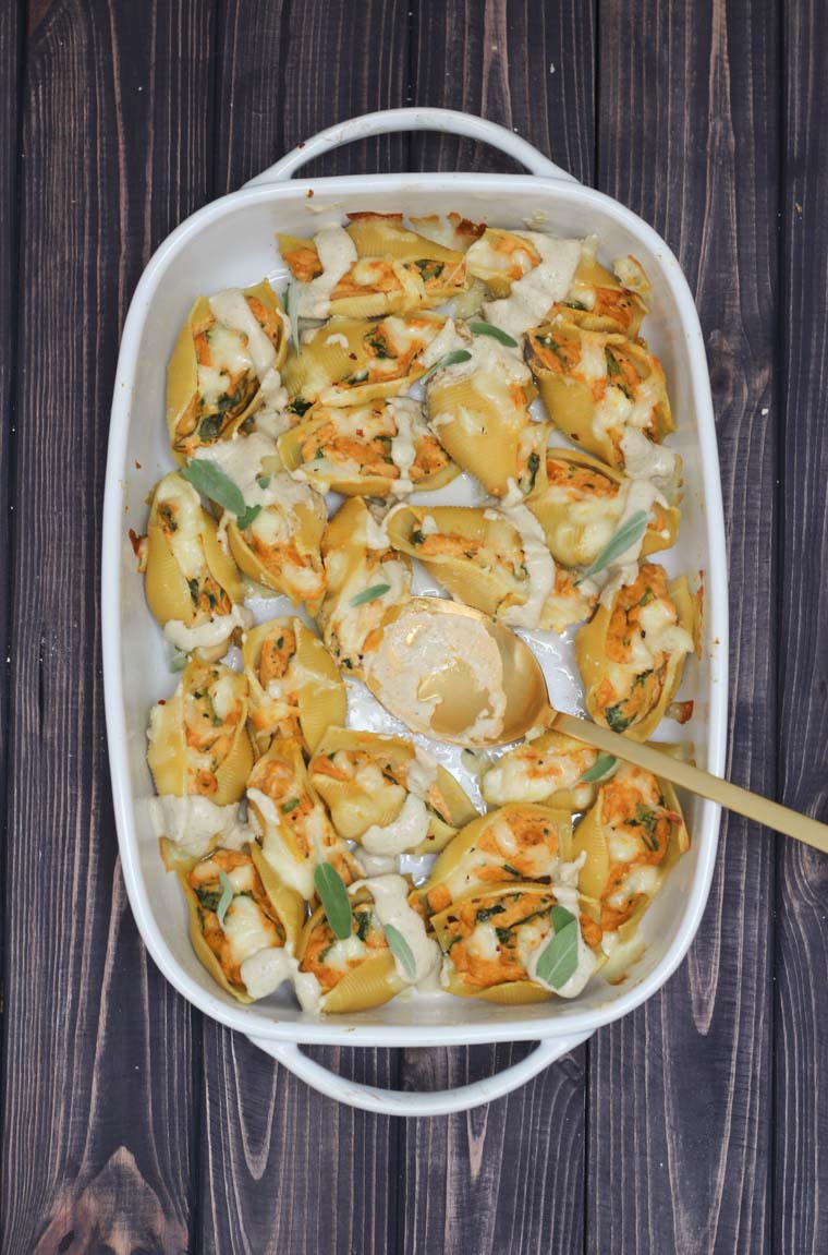 birds eye view Vegan holiday pasta in a white casserole dish with a golden spoon inside.