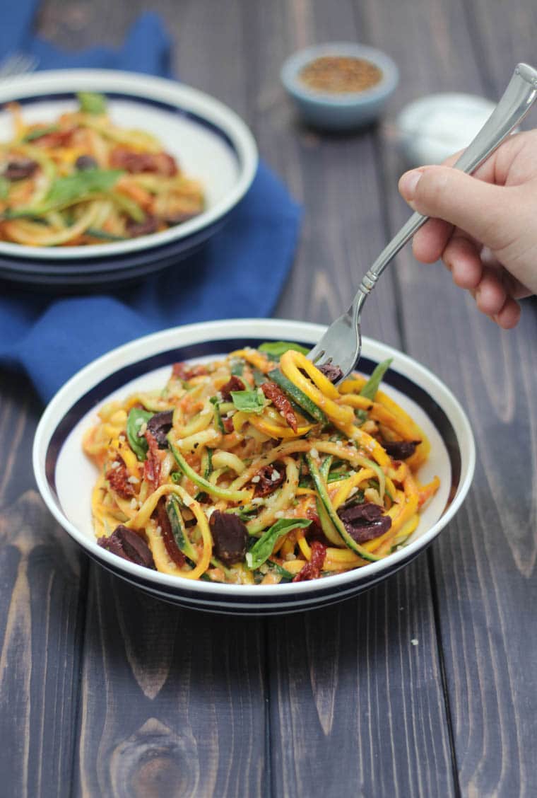 hand holding a fork in a black and white bowl of zucchini pasta with vodka sauce