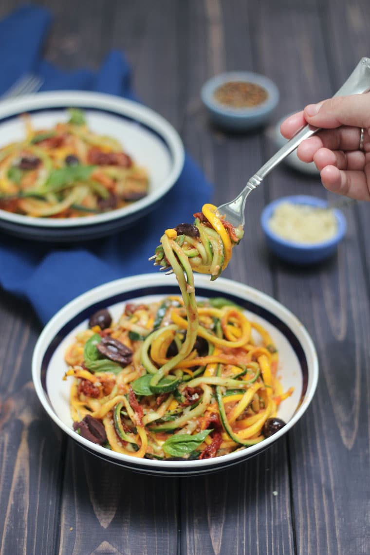 fork taking a bite out of low carb vegan zucchini noodle dish in a black and white bowl