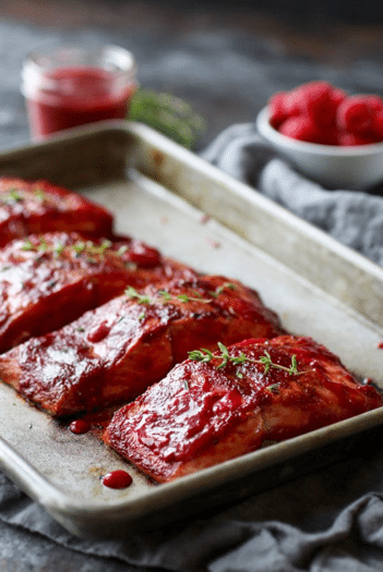 sheet pan containing a row of paleo raspberry balsamic glazed salmon filets topped with fresh herbs