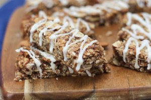 A close up image of multiple cinnamon bun granola bars on a brown cutting board.