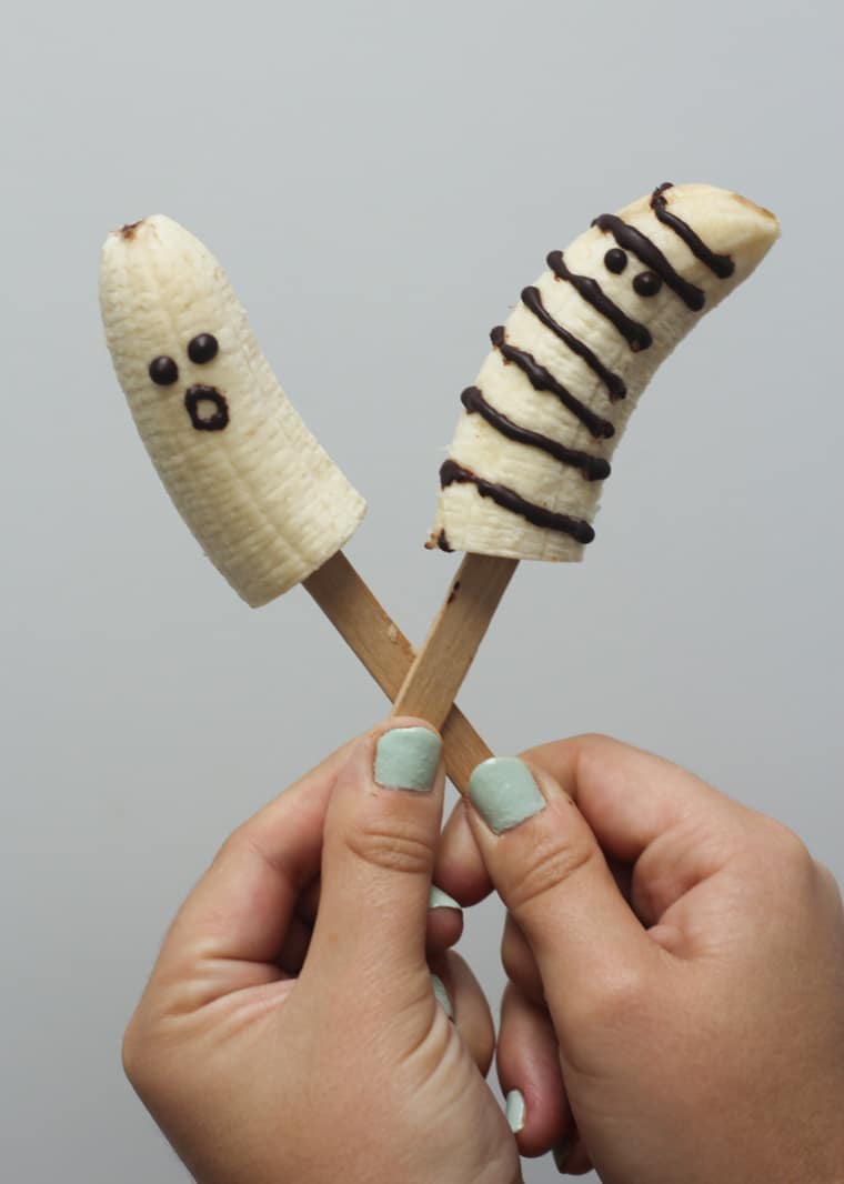 person holding halloween banana ghosts on two popsicle holders