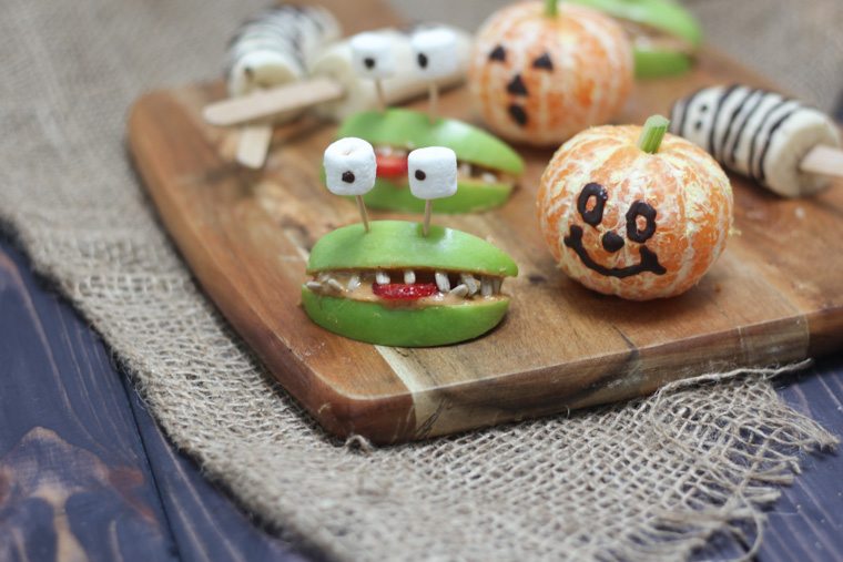 close up of various halloween themed fruit treats on a wooden serving board