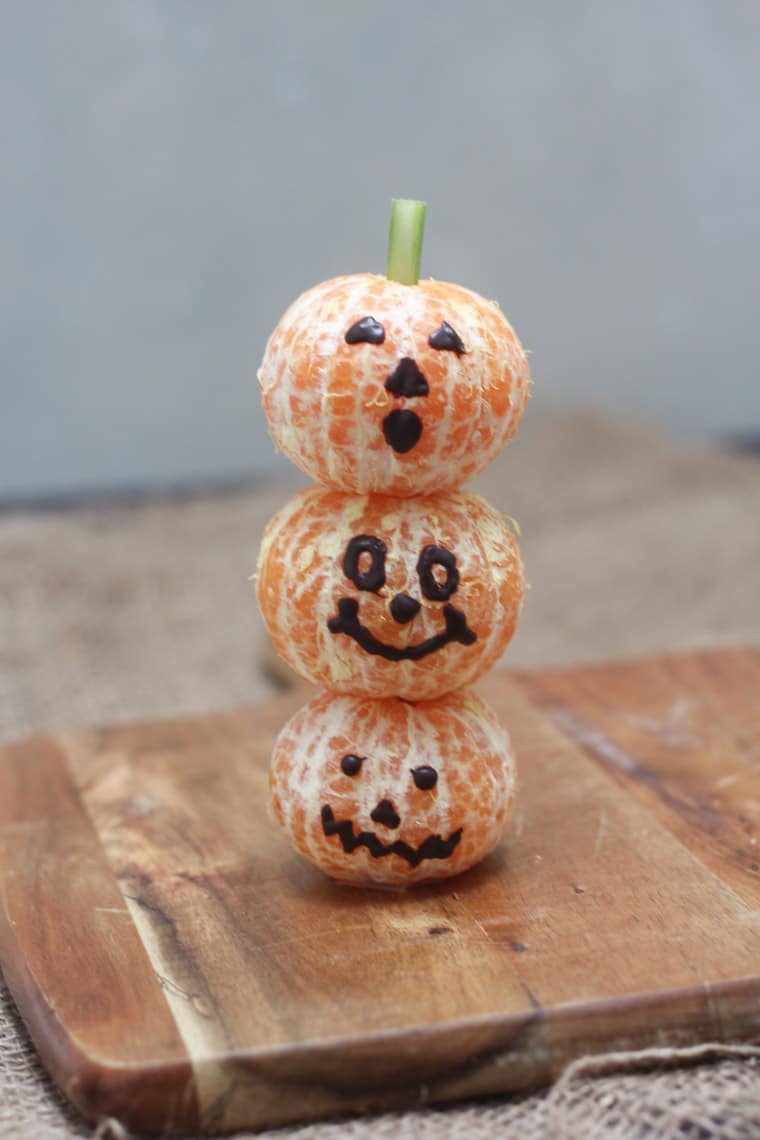 stack of halloween themed clementines on a wooden board