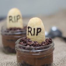 A close up of a Halloween graveyard mousse with an edible gravestone saying RIP in chocolate with a second one in the background.