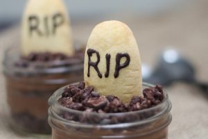 A close up of a Halloween graveyard mousse with an edible gravestone saying RIP in chocolate with a second one in the background.