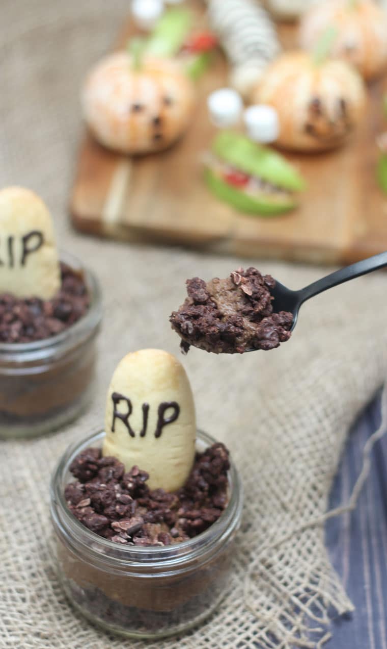 A close up of a spoon taking out a spoonful of Halloween graveyard mousse with an edible gravestone saying RIP in chocolate.