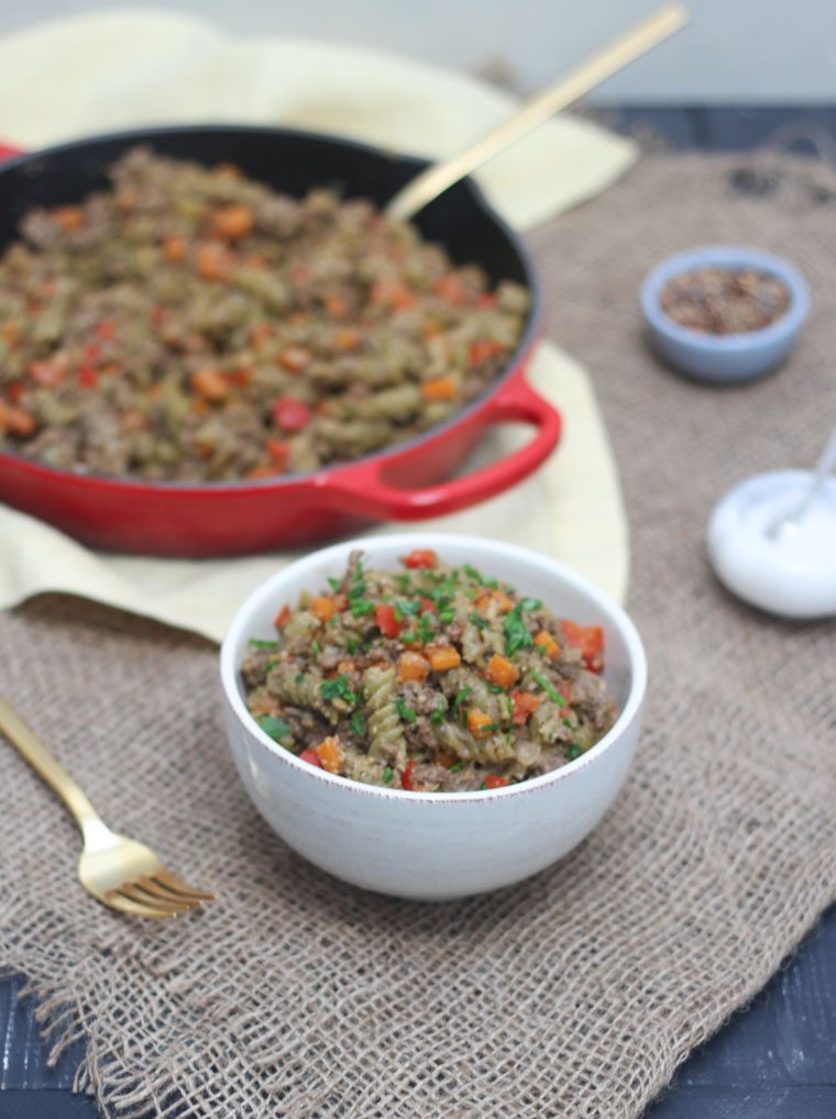 An angled image of a bowl of vegan hamburger helper in a white bowl with a red skillet in the background.