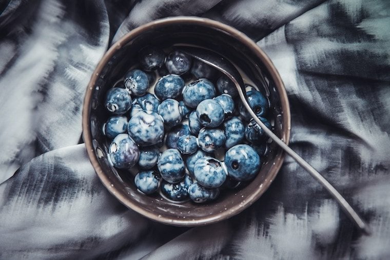 Close up of a bowl of fresh blueberries with a silver spoon.