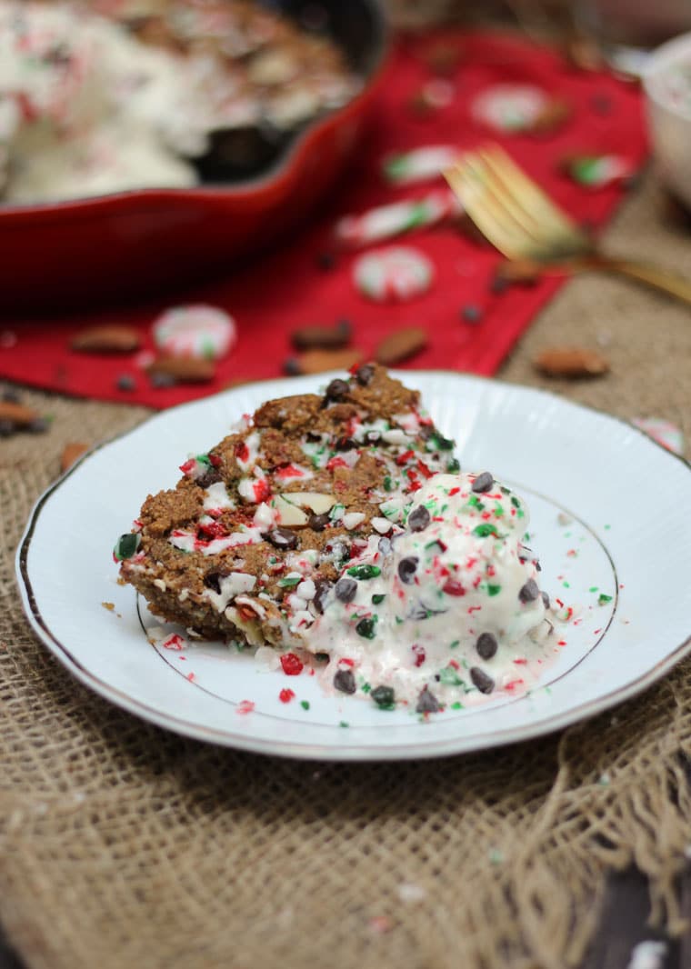 Slice of large cookie served on a white plate topped with ice cream. 